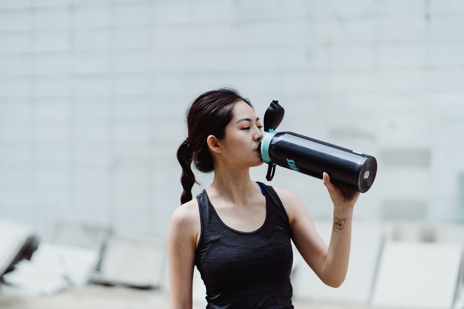 Jonge vrouw in sportkleding drinkt uit een waterfles, passend bij een gezonde levensstijl