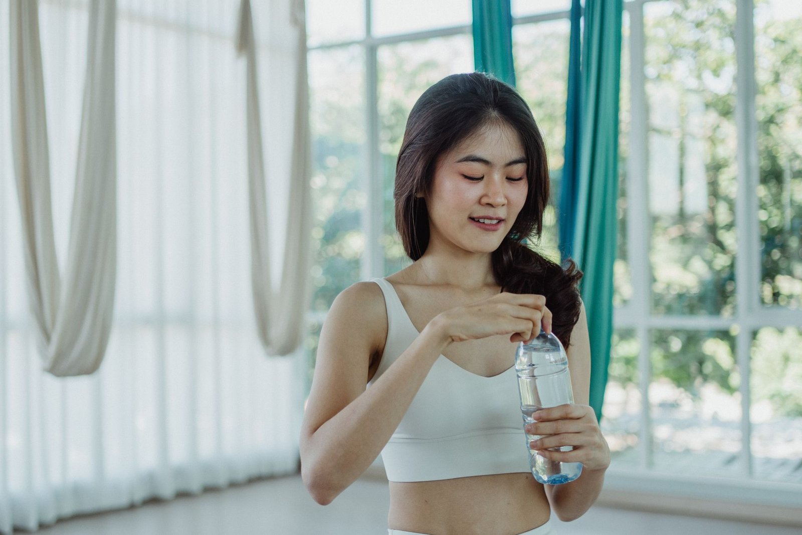 Vrouw in sportkleding houdt een waterfles vast in een lichte, luchtige sportschool